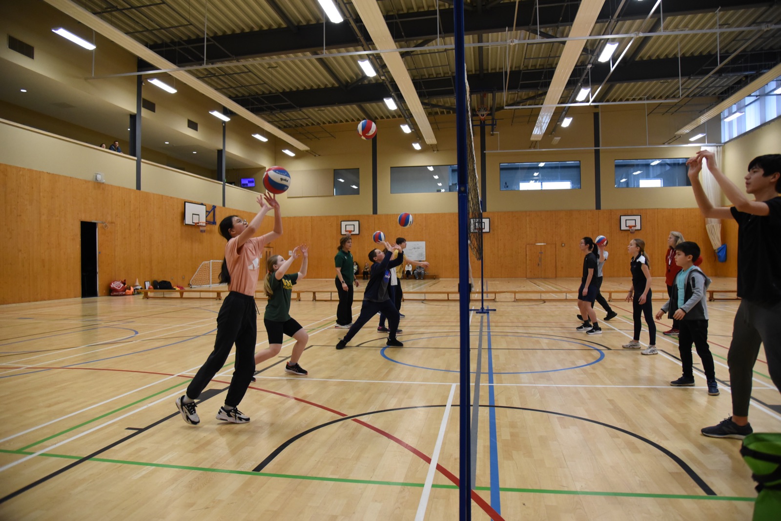 Young players practising volleyball skills together across a net in an indoor sports hall.